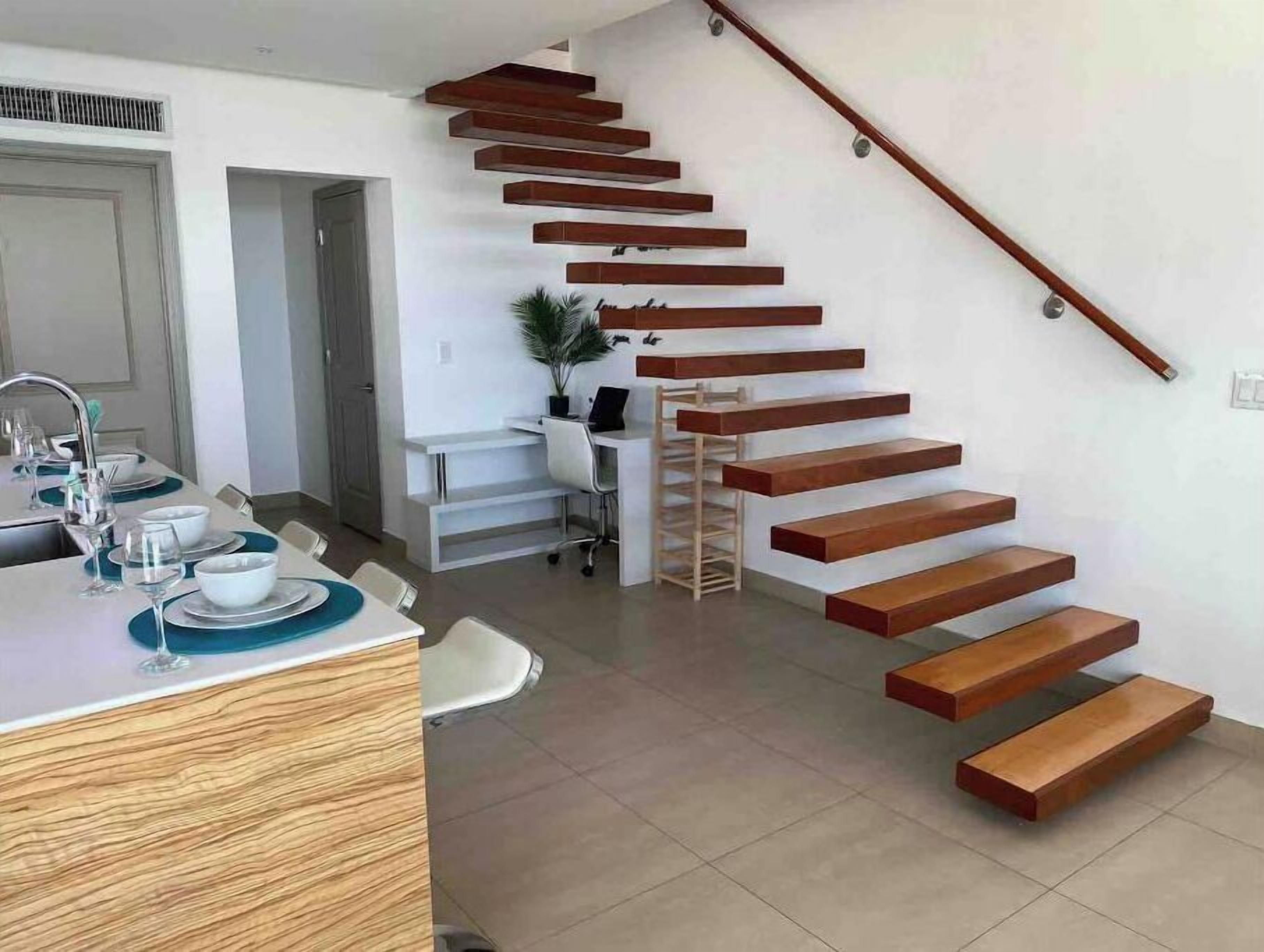 Una cocina moderna con comedor, una escalera de peldaños de madera y un pequeño espacio de oficina.