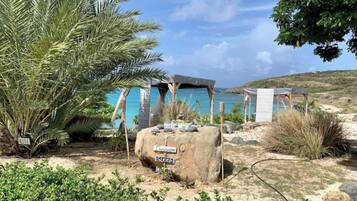 A beachside resort with a large palm tree, a rock with 'Massage' and 'Sleep' signs, and a small structure with a blue roof.