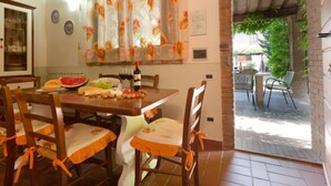 A dining area with a wooden table, chairs with orange cushions, a bottle of wine, and a watermelon on the table. - Girasole by Interhome (Peccioli)
