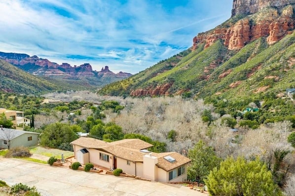 A residential area with houses surrounded by greenery and mountains in the background.