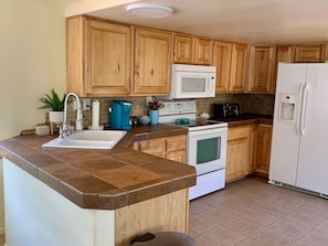 A kitchen with wooden cabinets, a white microwave, a stove, and a refrigerator.