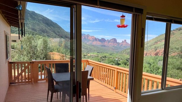 A wooden deck with a table and chairs, large windows offering a view of red rock formations and greenery. - Your Sedona Red Rocks Escape at Oak Creek Canyon! (Sedona)