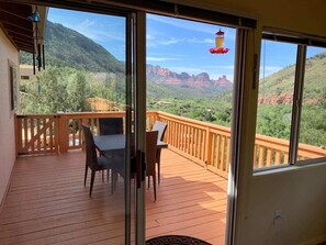 A wooden deck with a table and chairs, large windows offering a view of red rock formations and greenery.