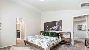 A bedroom with a bed, a nightstand, a wall-mounted shelf, and a door leading to another room. - Private Wine Country Retreat | South Nampa | Sleeps 10 (Nampa)