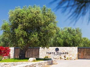 A stone wall with a wooden gate and a sign that reads "Porto Cesario Camping".