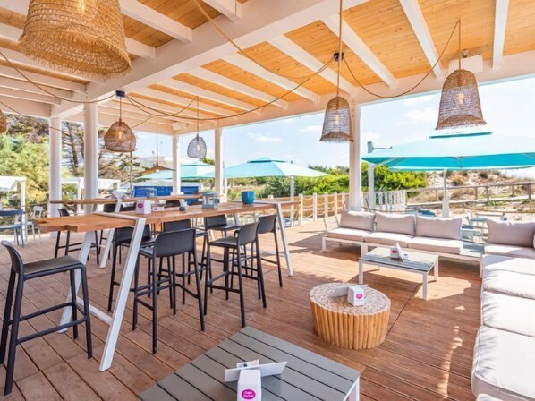 An outdoor patio with wooden flooring, tables, chairs, and hanging wicker lamps.