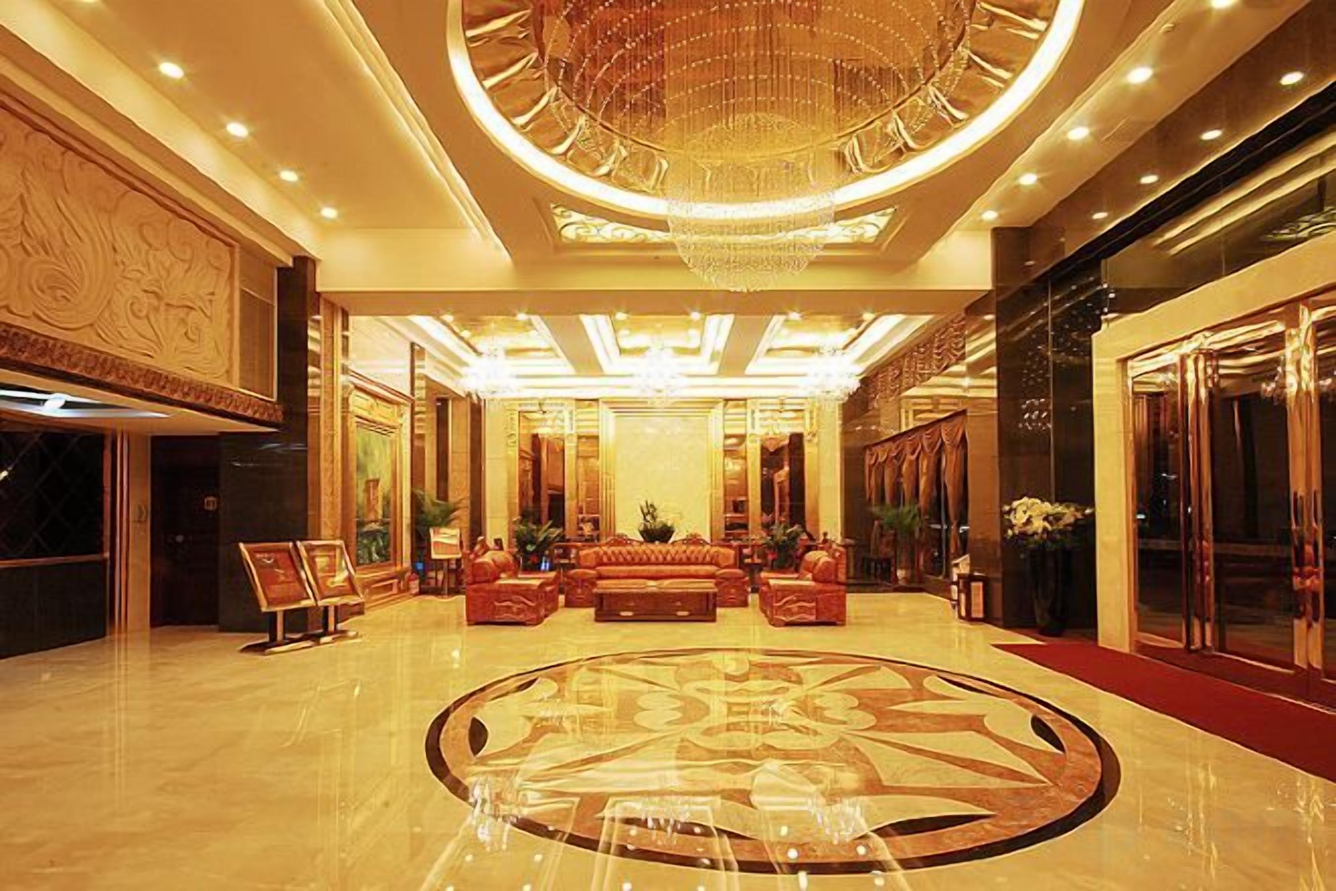A spacious lobby with a grand chandelier, a central seating area, and a polished floor.