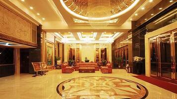 A spacious lobby with a grand chandelier, a central seating area, and a polished floor.