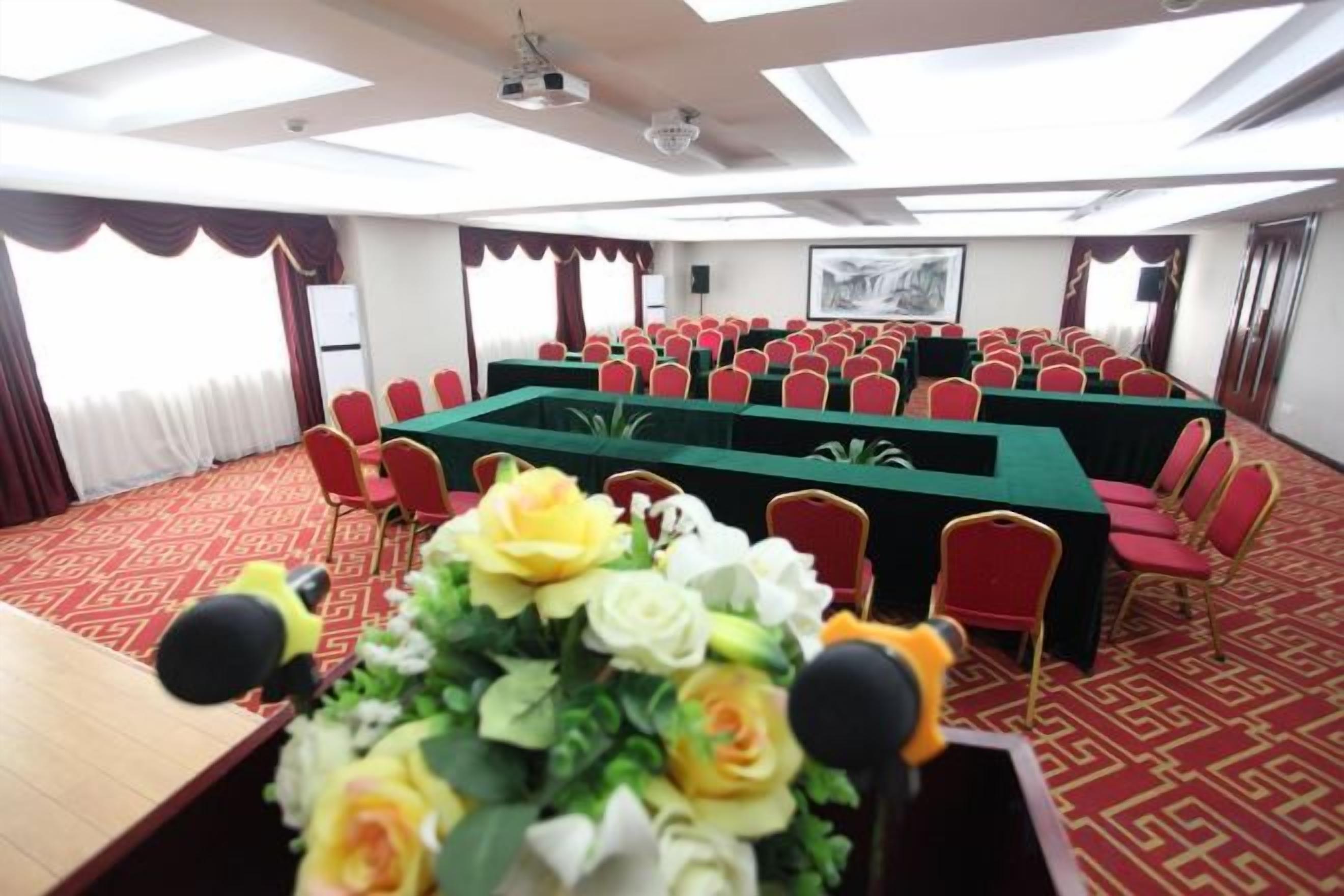 Sala de conferências com uma mesa comprida, cadeiras vermelhas e um arranjo floral.