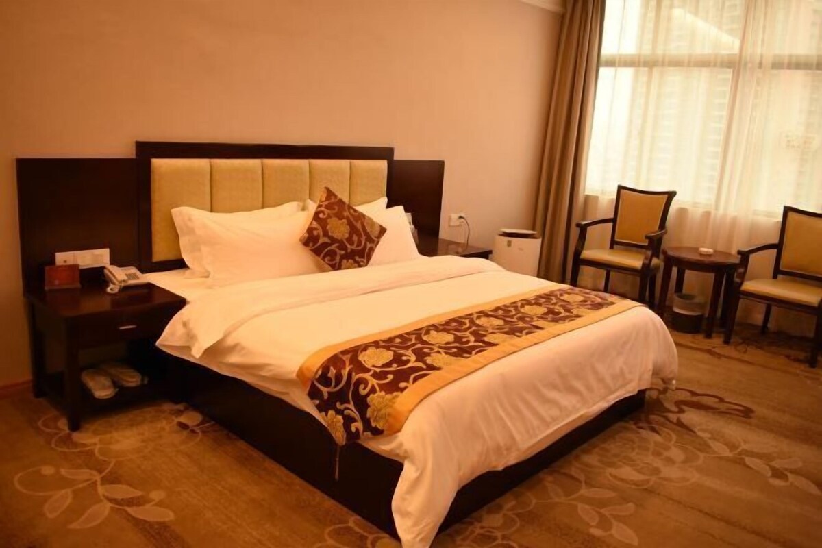 A hotel room with a large bed, a nightstand with a phone, and a seating area with two chairs and a small table.