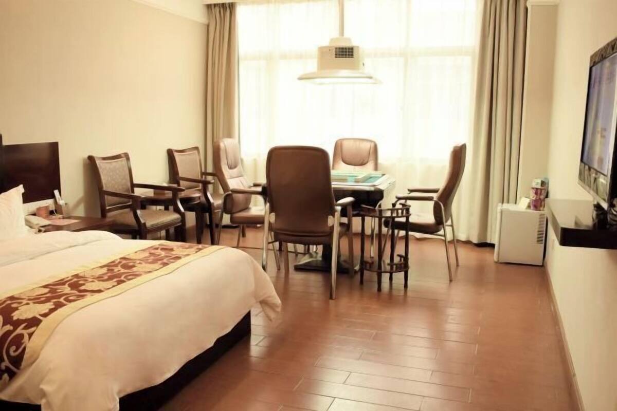 Una habitación de hotel con cama, escritorio con sillas, televisor y ventana con cortinas.