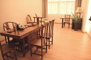 A dining area with a wooden table and chairs, a sofa, and a potted plant. - Jinjue Hotel (Nearby Train Station) (Huizhou)