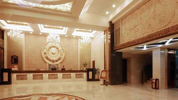Een hotel lobby met een receptiebalie, een grote decoratieve wand en een kroonluchter.