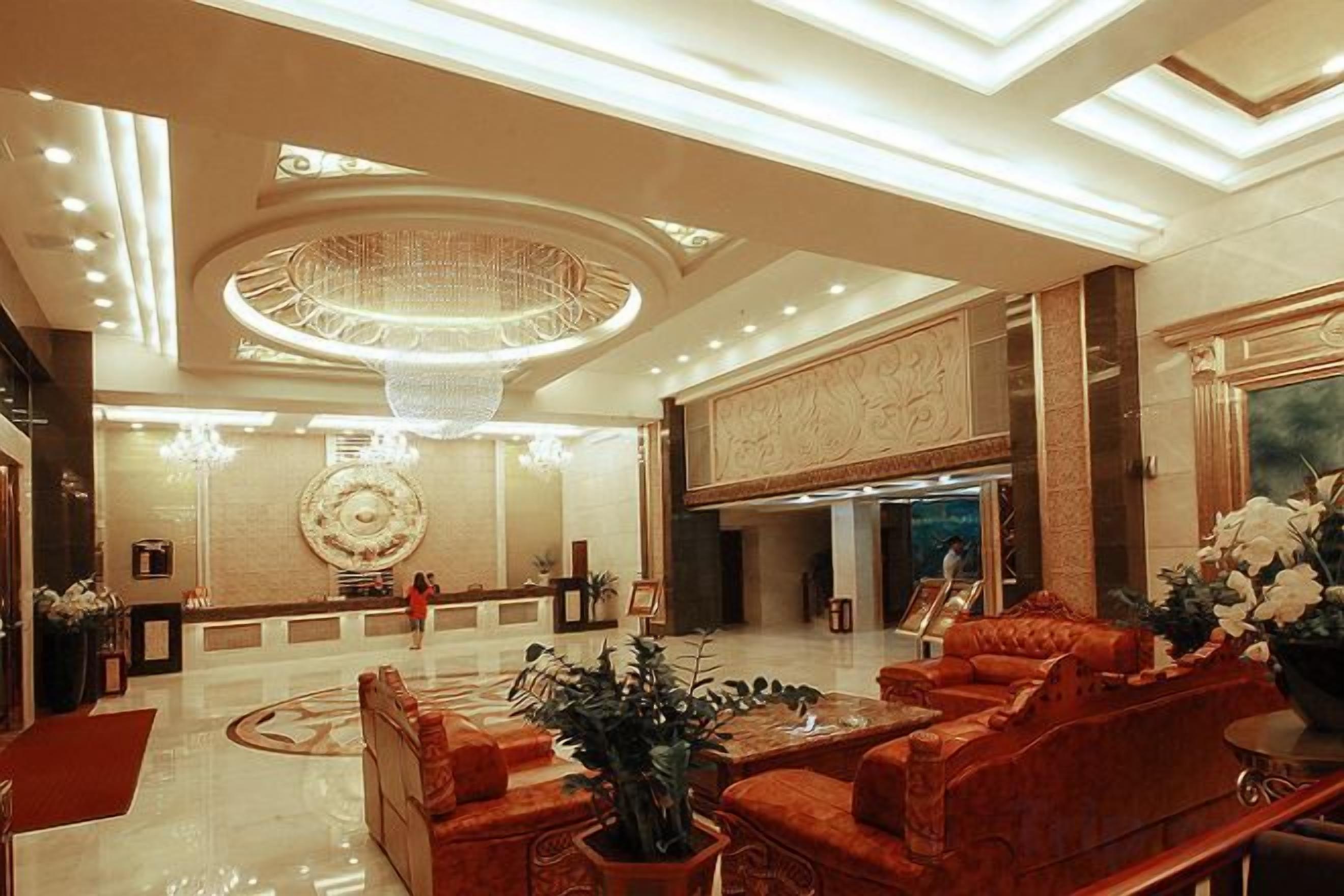 Un hall d’entrée spacieux, agrémenté d’un magnifique lustre, d’un comptoir de réception et d’un espace détente avec des canapés rouges.