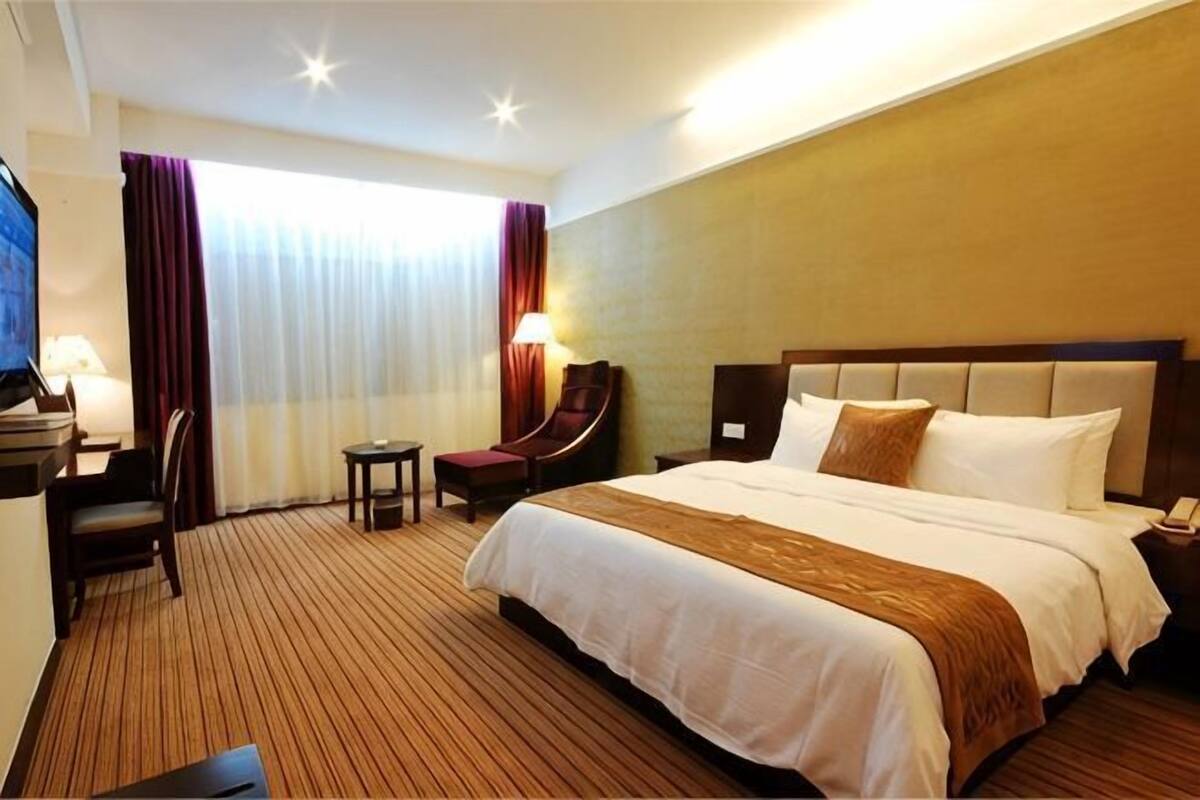 Habitación de hotel con una cama grande, un escritorio con silla, una mesita y un televisor.