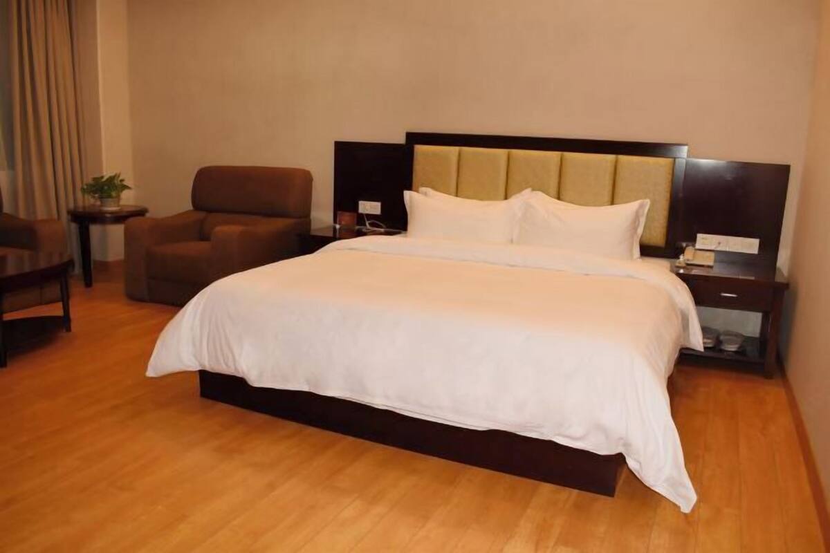 Una habitación de hotel con una cama grande, una silla, una mesita pequeña y una mesita de noche.