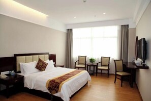 A hotel room with a large bed, two chairs, a small table, a TV, and a window with curtains. - Jinjue Hotel (Nearby Train Station) (Huizhou)