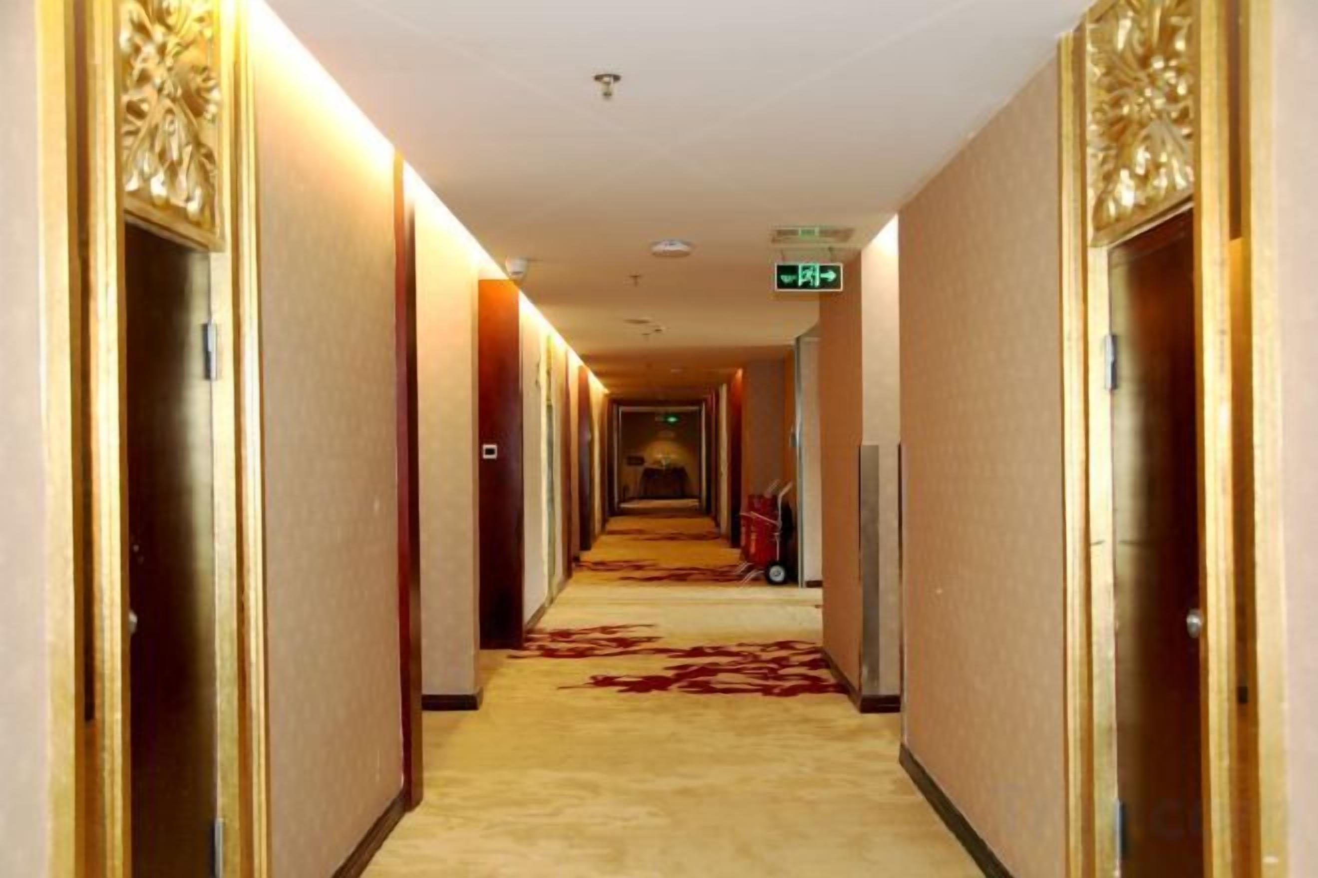 En hotellkorridor med dörrar på båda sidor, ett heltäckningsmatta och en skylt som är monterad på väggen.