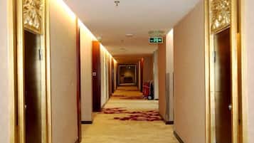 En hotellkorridor med dörrar på båda sidor, ett heltäckningsmatta och en skylt som är monterad på väggen.