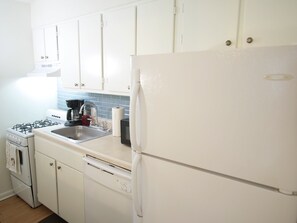 Una cocina con armarios blancos, estufa, pileta, refrigerador y lavavajillas.