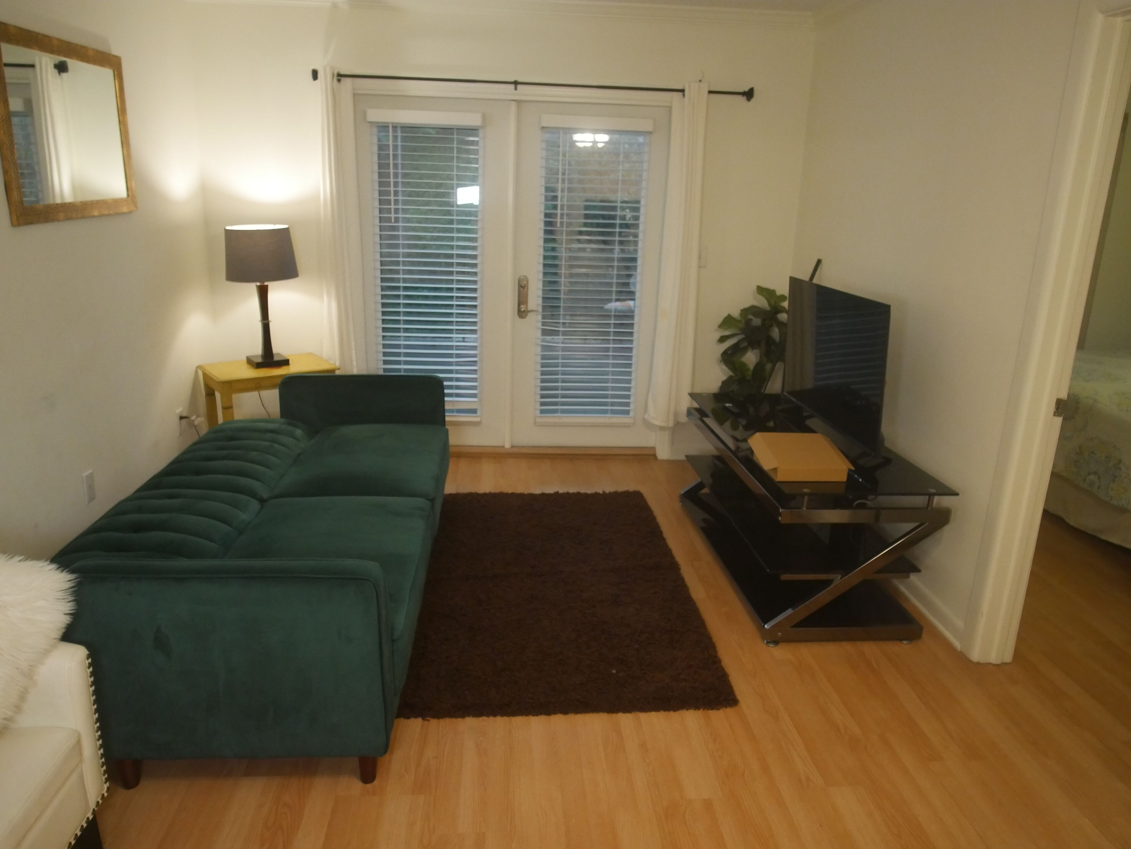 Ein Wohnzimmer mit einem grünen Sofa, einem braunen Teppich, einem Fernseher auf einem Schrank und einer Schiebetür.