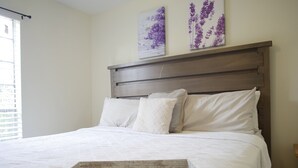 Ein ordentlich bezogenes Bett mit einem hölzernen Tablett davor, einem Kopfteil und zwei an der Wand hängenden floralen Bildern.