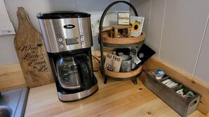 Una cafetera, un letrero de madera, una taza y una bandeja con objetos sobre una encimera de madera.
