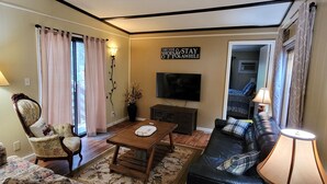 Una sala de estar con sofá, sillón, mesa, televisor y un letrero en la pared.