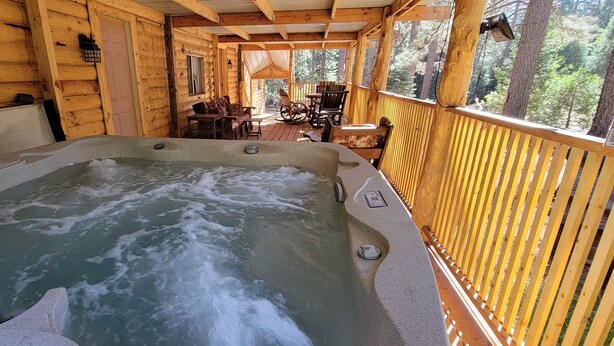 Una cabaña de madera con un jacuzzi en la terraza, rodeada de paredes de madera y vistas a un bosque.