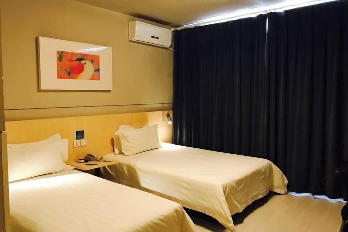 A hotel room with two beds, a painting on the wall, and a window with curtains.