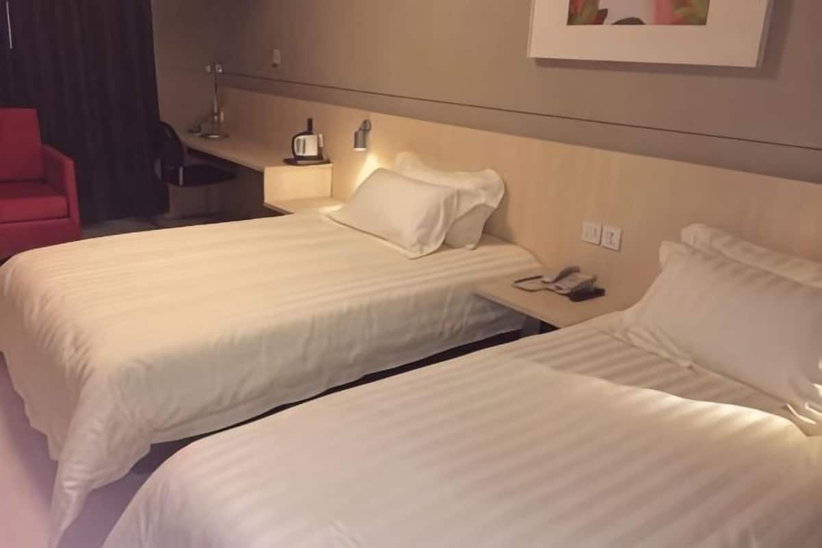 Two single beds with white linens, a bedside table with a lamp, and a red chair.