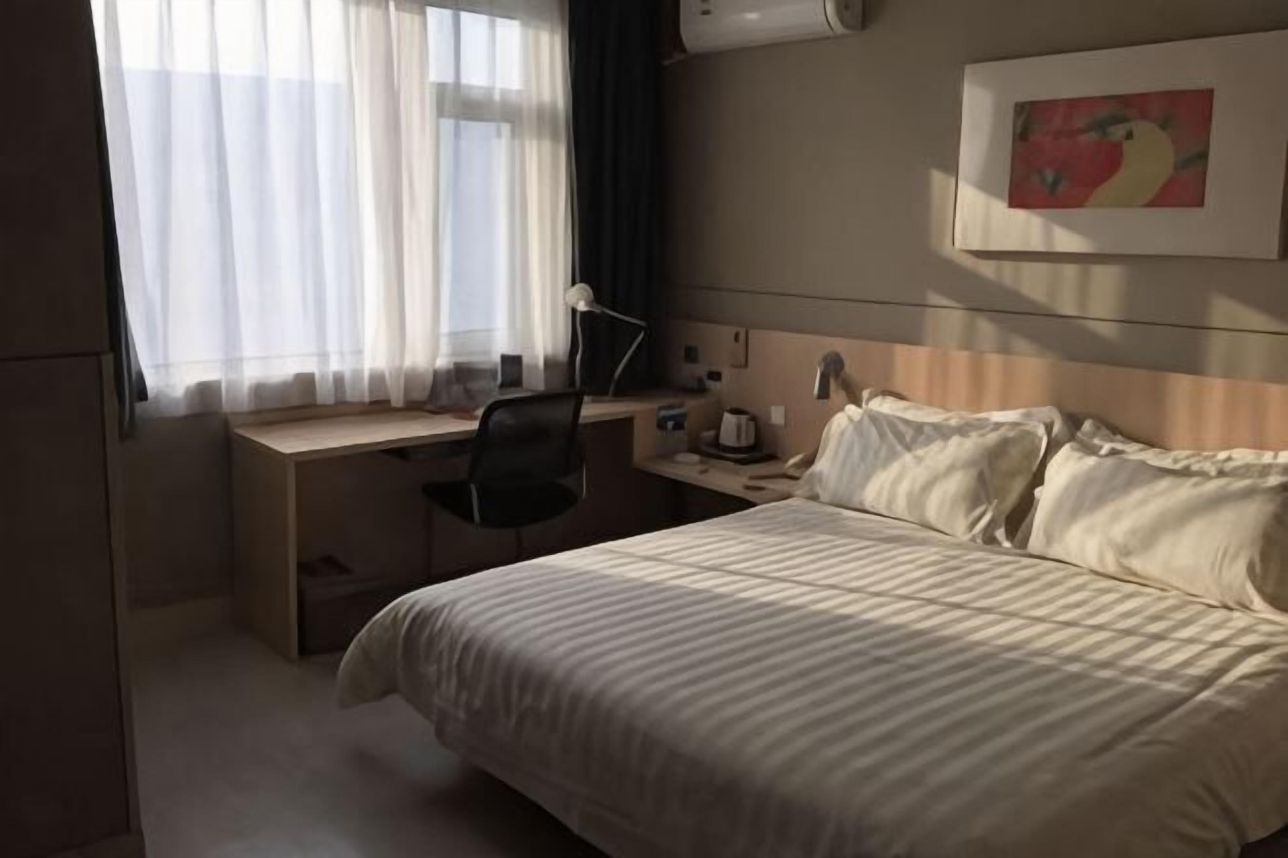 A hotel room with a bed, desk, chair, and a painting on the wall.