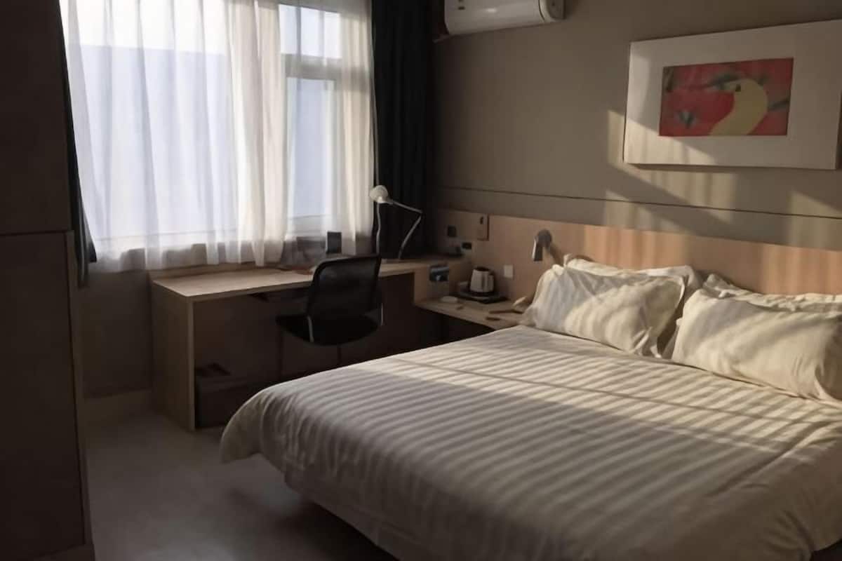 A hotel room with a bed, desk, chair, and a painting on the wall.