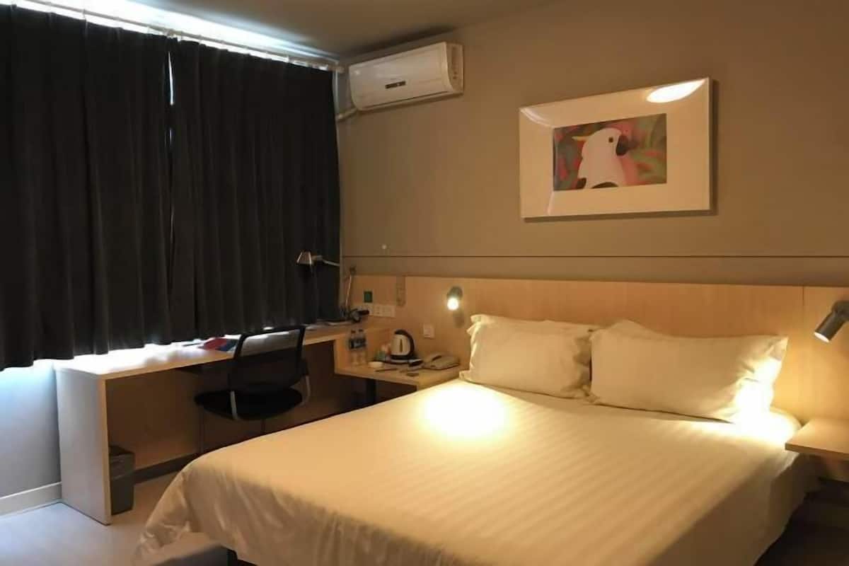A hotel room with a bed, desk, chair, and an air conditioning unit.