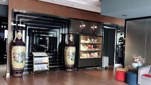 A modern lobby with a reception desk, two large vases, a bookshelf, and a seating area with colorful stools. - Jincheng Hotel (Bazhou Shengfang Town) (Bazhou)