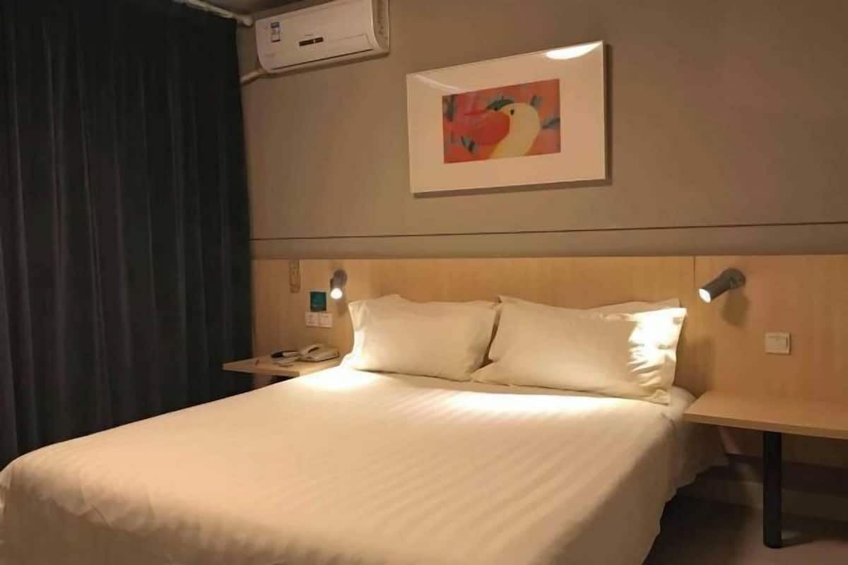 A hotel room with a bed, a nightstand, a lamp, and a painting on the wall.