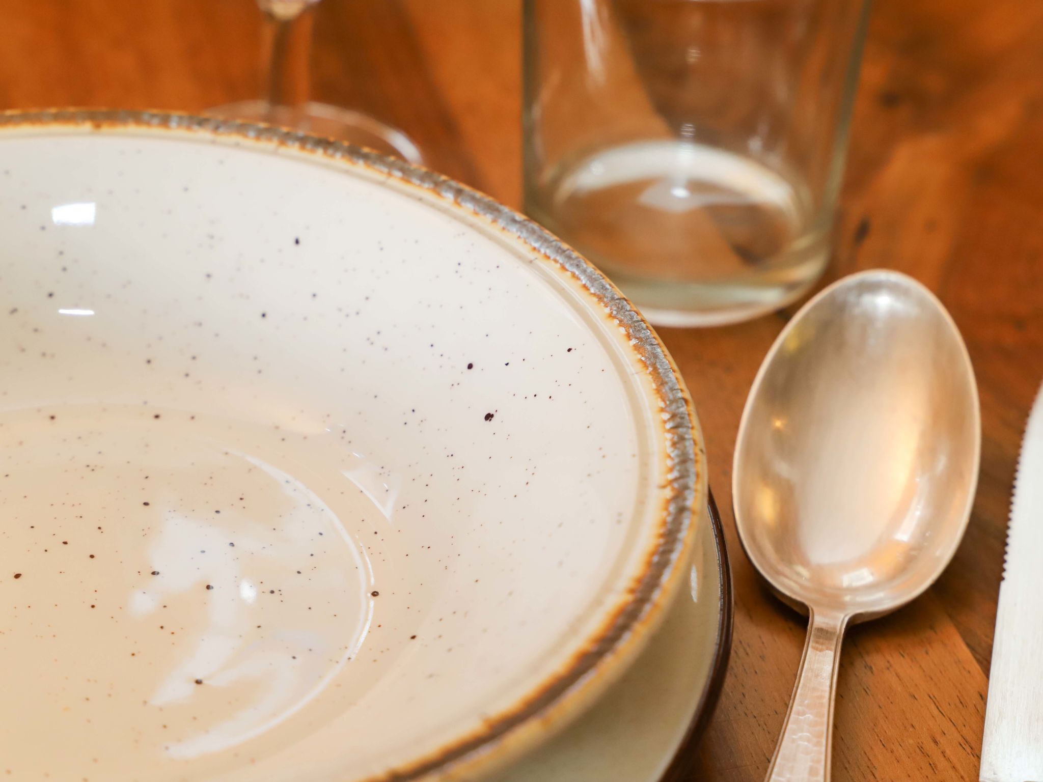 A ceramic plate with a speckled design, a clear glass, and a metal spoon on a wooden table.