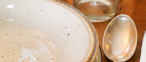 A ceramic plate with a speckled design, a clear glass, and a metal spoon on a wooden table.