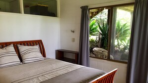 A bedroom with a wooden bed, a small bedside table, and a window with curtains. - Whiritoa -Glorious Beach Front! (Whiritoa)