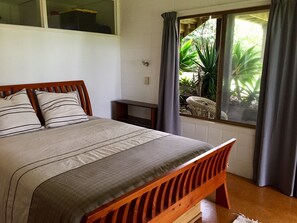 A bedroom with a wooden bed, a small bedside table, and a window with curtains.