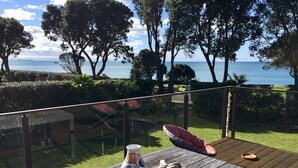 A wooden deck with a table, a vase, and a paddle. - Whiritoa -Glorious Beach Front! (Whiritoa)