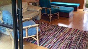A cozy living room with a sofa, two armchairs, a colorful striped rug, and a large window with a view of the outdoors. - Whiritoa -Glorious Beach Front! (Whiritoa)