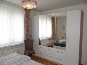 Una camera da letto con un letto, una sedia, un armadio e uno specchio.