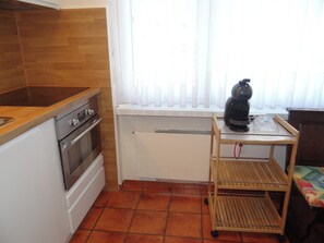 Una cucina compatta con piano cottura, forno e una finestra con persiane.