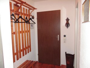 Una porta in legno con maniglia metallica, un attaccapanni con grucce, un piccolo cestino e un lampadario a parete.