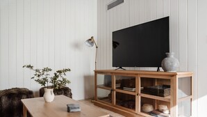 A living room with a wooden table, a TV on a stand, a plant, and a cabinet with shelves. - NEW: Charming Desert Abode! Centrally located, near UofA & downtown Tucson (Tucson)