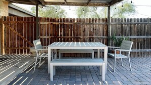 A covered patio area with a table and chairs, a wooden fence, and string lights. - NEW: Charming Desert Abode! Centrally located, near UofA & downtown Tucson (Tucson)
