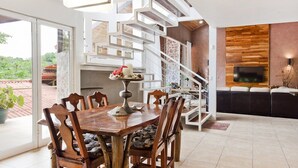 A modern dining area with a wooden table and chairs, a white staircase, and a TV mounted on a wooden wall. - Tropical Treehouse with Private Pool - 3BR/2.5B (Manuel Antonio)