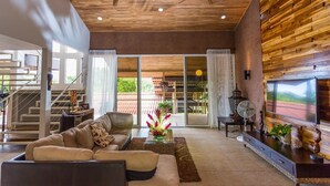 A modern living room with a sofa, coffee table, and TV. There is a staircase leading to a balcony with outdoor furniture. - Tropical Treehouse with Private Pool - 3BR/2.5B (Manuel Antonio)