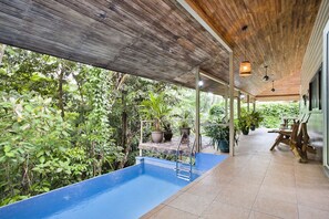 An indoor swimming pool with a wooden ceiling and tiled floor, surrounded by lush greenery. - Tropical Treehouse with Private Pool - 3BR/2.5B (Manuel Antonio)